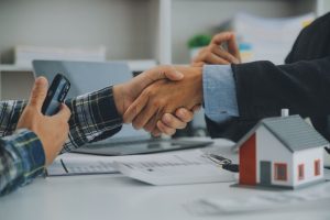 Ein Makler und sein Kunden sitzen am Schreibtisch und geben sich die Hand