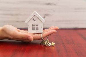 Eine Person hält ein Miniaturhaus und einen Schlüssel in der Hand